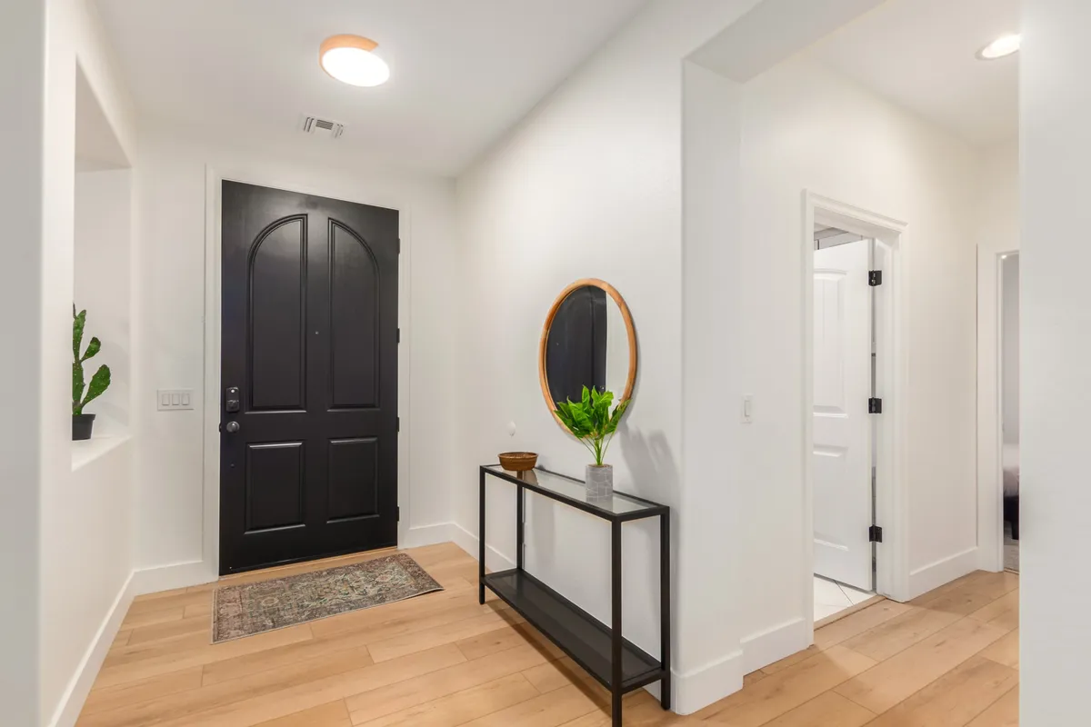An inviting entryway with a black front door, circular mirror, and a console table decorated with a plant. The scene is well-organized and gives a sense of order, tidiness, and a warm welcome.