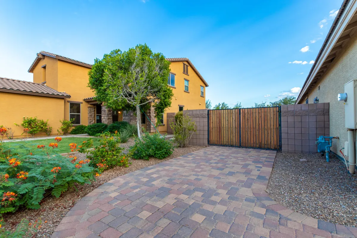 A picturesque backyard garden with vibrant flowers, a paved pathway, and a wooden gate that opens to a lush, expansive lawn. The two-story house in the background and abundant greenery make it perfect for children’s games, outdoor parties, and evening relaxation.