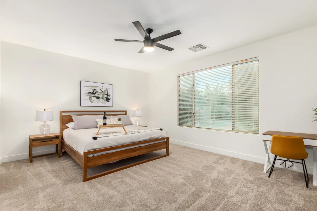 A tranquil bedroom with a bed, window, desk, and artwork. Natural light filters in, emphasizing a serene, restful ambiance ideal for relaxation, reading, or quiet work.