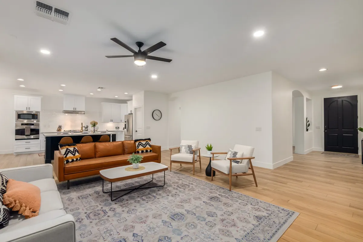 A modern, tastefully decorated living room featuring a comfortable sofa, stylish chairs, a coffee table, an area rug, and a direct view into the kitchen. The space is softly lit, with inviting tones and a layout conducive to both relaxation and intimate social gatherings.