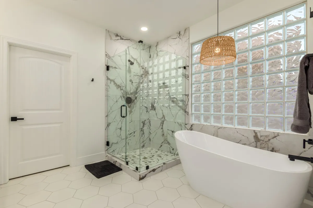 A luxurious bathroom showcases a freestanding bathtub, a glass-enclosed shower, marble walls, and a contemporary hanging light fixture. The ambiance is spa-like, with elegant finishes and cozy lighting designed for relaxation.
