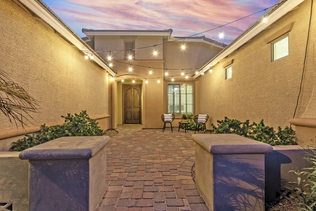 An inviting outdoor seating area illuminated by string lights, with comfortable chairs and a pathway of pavers, set for evening relaxation or socializing with friends.