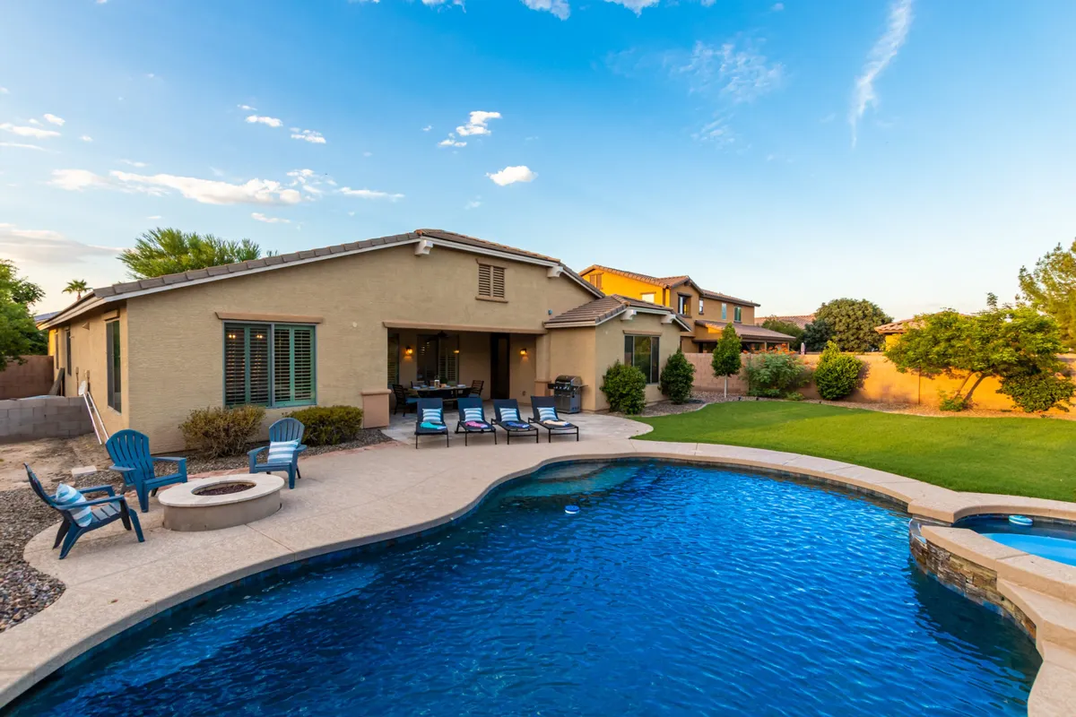 An exterior view of a serene swimming pool, fire pit seating area, and a lush green lawn. The inviting patio space is ideal for both tranquil afternoon lounging and celebratory evening gatherings, highlighting the flexibility and comfort of the private outdoor amenities.