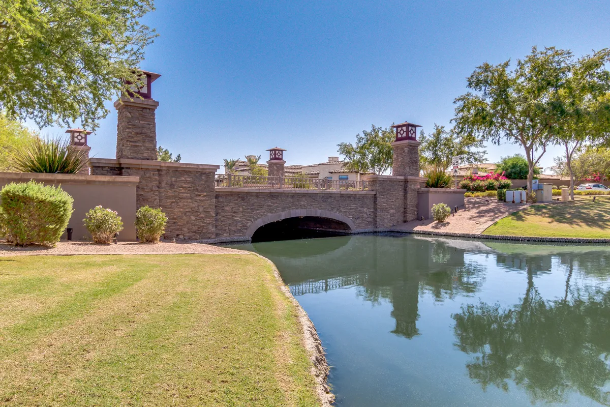 A picturesque stone bridge spans a reflective water surface surrounded by lush greenery, evoking the tranquil, manicured environments that define top-tier golf clubs. The scene is serene and inviting, suggesting a refined outdoor experience similar to what visitors might enjoy at or near the Ocotillo Golf Club.