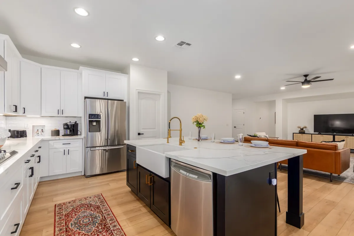 A stylish kitchen space featuring a central island with spacious seating, stainless steel appliances, a modern faucet, and a decorative rug. The layout provides a clear view into the living room, emphasizing a sense of community and shared experience.