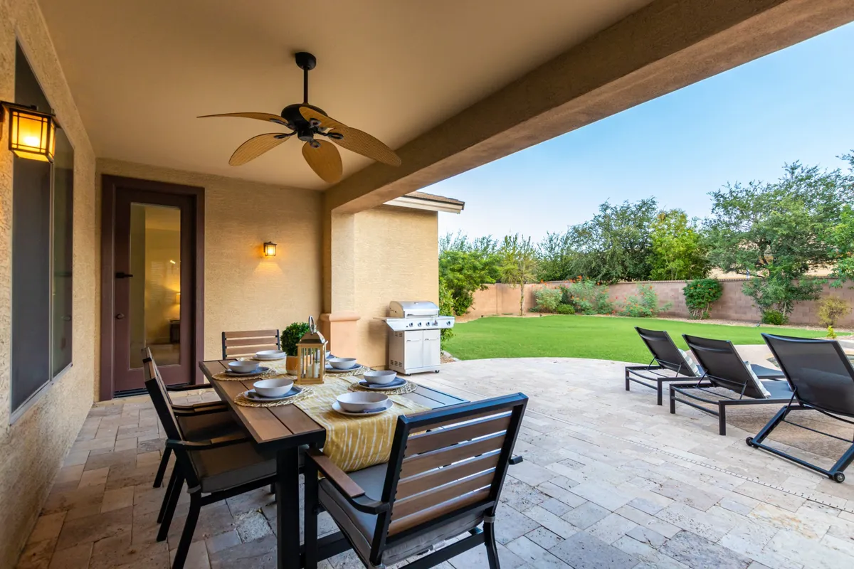 This exterior image displays an inviting outdoor dining area with a table set for meals, a nearby grill for barbecuing, a lush lawn, and loungers by the pool. The ambiance is casual yet sophisticated, offering a seamless flow between entertaining, dining, and relaxing under open skies.