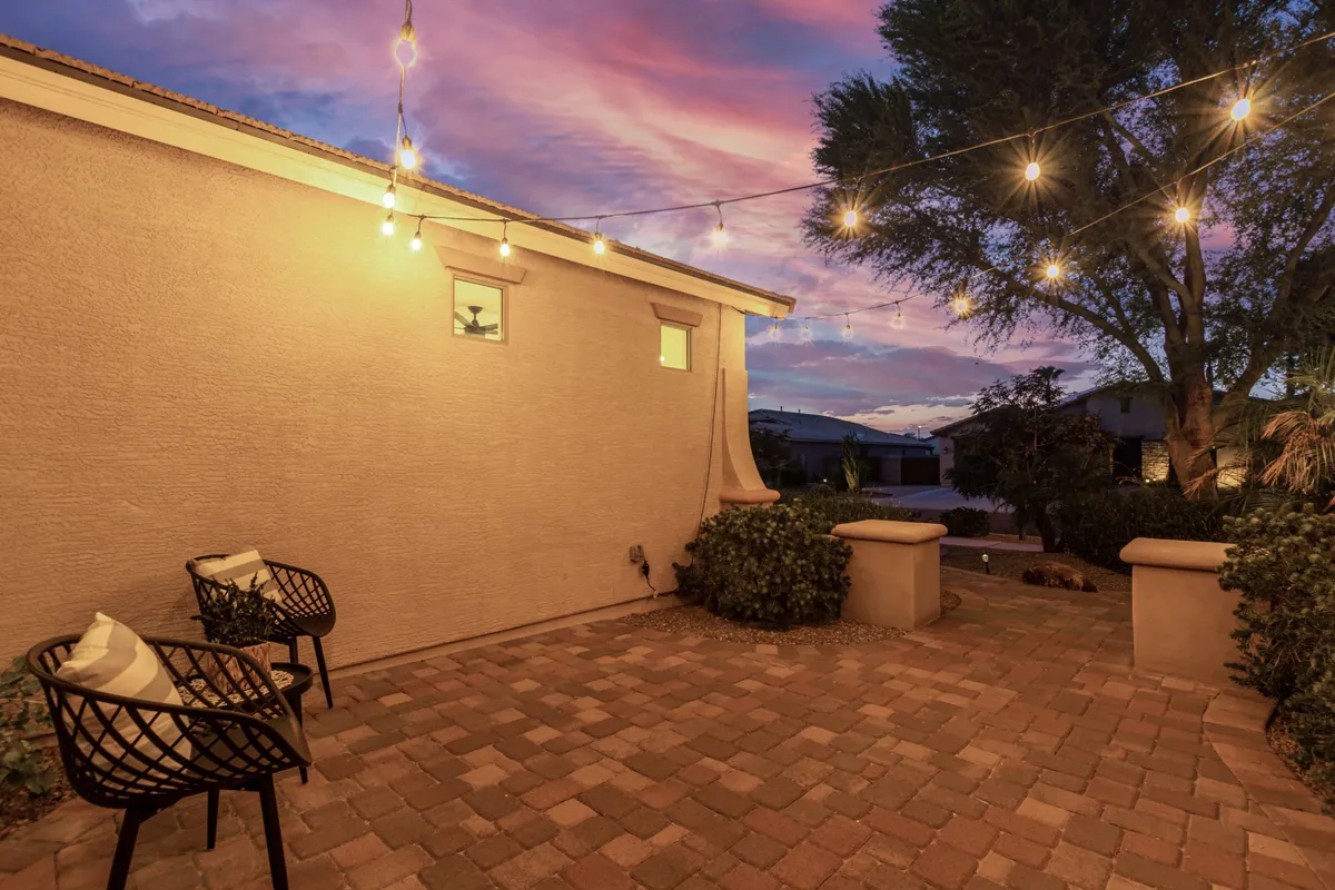 This image depicts a relaxed and inviting patio area featuring string lights, a paved surface, and comfortable seating. The scene is set for evening gatherings, with the soft glow of lights creating an intimate ambiance perfect for socializing or unwinding after a night out. The outdoor living space seamlessly connects the home to the surrounding environment, inviting residents and guests to enjoy the mild Arizona evenings.